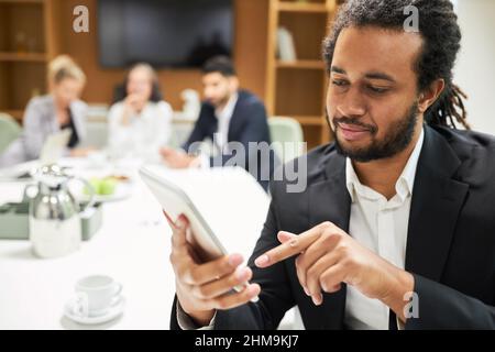 Business man typing text message on smartphone with team in conference room in background Stock Photo