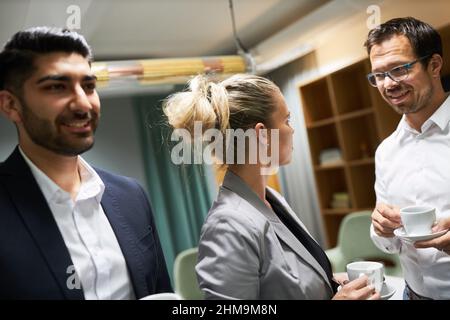 Three business people having small talk during the break in the office drinking a cup of coffee together Stock Photo