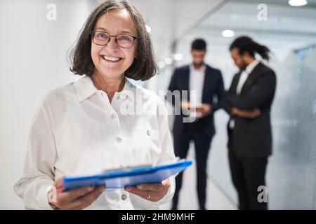 Happy senior businesswoman with a contract or memo on clipboard in the office hallway Stock Photo