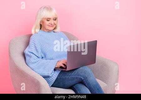 Portrait of attractive focused grey-haired woman using laptop writing e-mail isolated over pink pastel color background Stock Photo