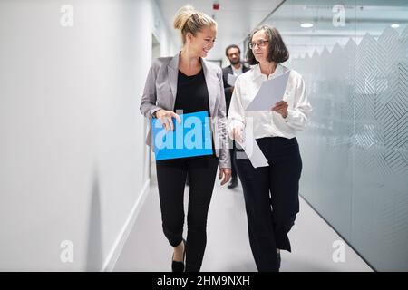 Two business women with documents are talking about a project or an assignment on the office corridor Stock Photo