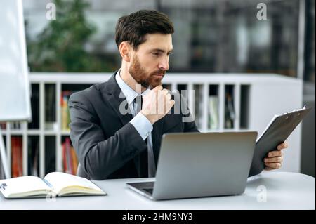 Focused successful caucasian business man in formal suit, company ceo, sits in the modern office, studies financial reports, analyzes profits, plans a strategy, develops a startup, thinking Stock Photo