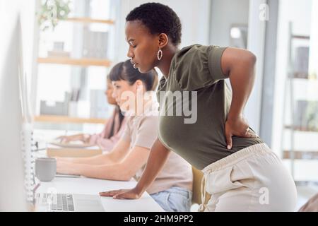 Ive been spending hours on this project. Shot of a businesswoman experiencing back pain while getting up from her desk. Stock Photo