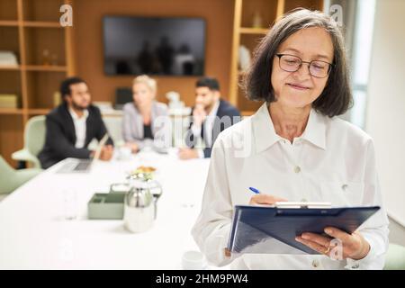 Senior businesswoman with clipboard and checklist making notes in business meeting Stock Photo