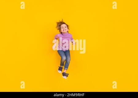 Full size photo of cheerful good mood little playful boy jumping up fooling around isolated on yellow color background Stock Photo