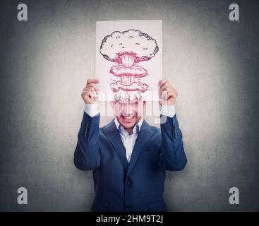 Irritated and stressed businessman holding a paper sheet over head imitating brain explosion. Annoyed person suffering headache. Mental health, migrai Stock Photo