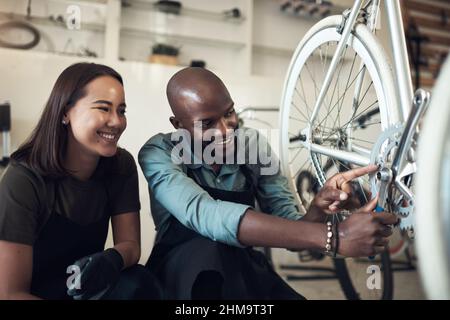 I fixed that. Shot of two young business owners crouching in their shop and fixing a bicycle wheel. Stock Photo