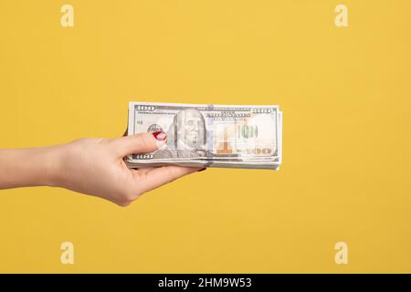 Profile side view closeup of woman hand holding and showing fan of american dollar money in hand. Indoor studio shot isolated on yellow background. Stock Photo