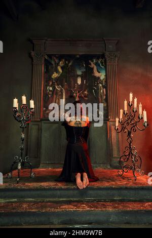 Prayer in church. Barefoot woman with dark hair kneeling in the Church, lights a candle and prays in front of the icon. Stock Photo