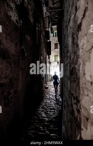 Young Woman Walks Alone Through Spooky Narrow Abandoned Alley In The Night Stock Photo