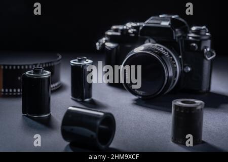 Film photography - a vintage metallic film cartridge and 35mm SLR camera against a dark background. Stock Photo