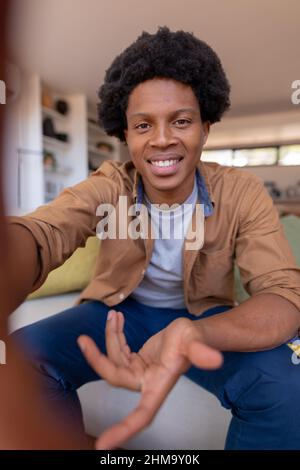 Portrait of smiling african american young man gesturing during video call while sitting at home Stock Photo