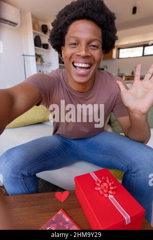 Portrait of cheerful african american young man waving during video call while sitting at home Stock Photo