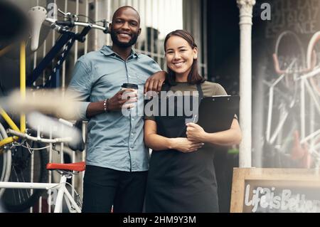 Lets get you the bike of your dreams. Shot of two young business owners standing outside their bicycle shop during the day. Stock Photo