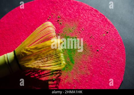 Top view of bamboo chasen and powdered dried matcha on pink circle on black table in sunlight Stock Photo