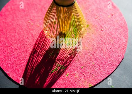 Bamboo chasen and powdered dried matcha on pink circle on black table in sunlight Stock Photo