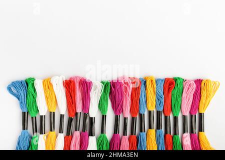 Line with many mixed vivid colored sewing threads for embroidery isolated on a white table, top view or flat lay of red, pink, yellow, blue and green Stock Photo
