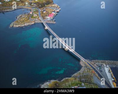 Drone view of long narrow bridge crossing calm clear sea on grassy Lofoten islands with buildings in nature of Norway Stock Photo