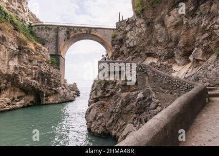 Old bridge with arched passage over rippling water located between rough rocky cliffs in nature of Italy in Fiordo de Furore region Stock Photo