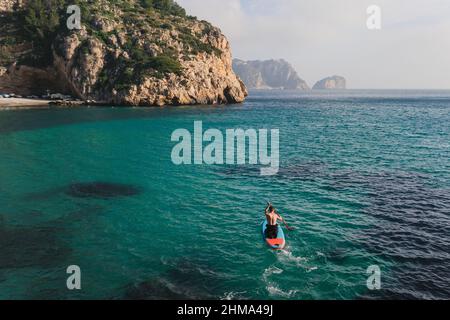 Side view of anonymous female in hat sitting in rock looking at hole in ceiling of cave near sea on sunny day in Algarve, Portugal Stock Photo