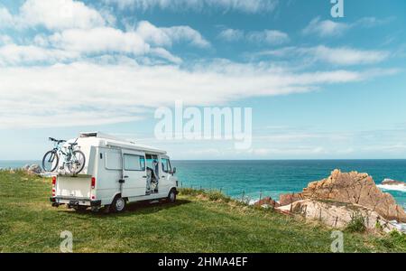 Border Collie dog sitting in camper van parked on hilly coast of blue sea during summer road trip in Cantabria Stock Photo