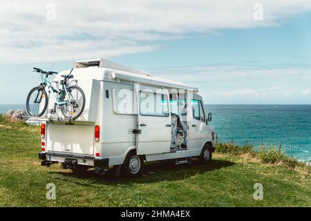 Border Collie dog sitting in camper van parked on hilly coast of blue sea during summer road trip in Cantabria Stock Photo