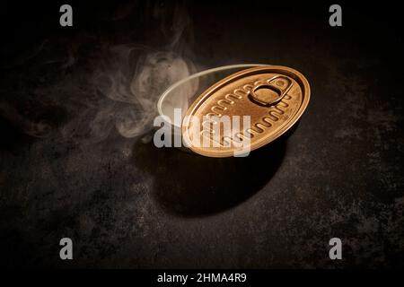 From above of empty tin can with opened lid placed on black background with smoke in room with dim light Stock Photo
