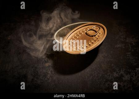 From above of empty tin can with opened lid placed on black background with smoke in room with dim light Stock Photo