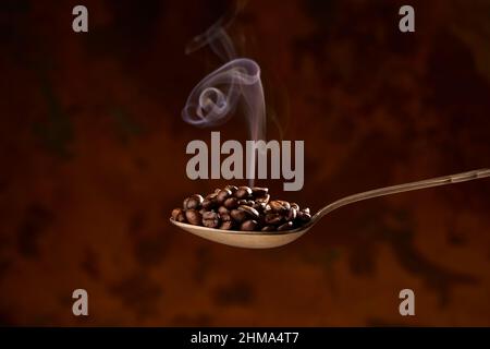 From above of closeup of spoon full of heap of roasted coffee beans on brown background Stock Photo