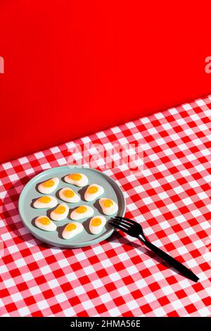 From above of plate with jelly eggs and fork placed on red checkered napkin against scarlet background Stock Photo