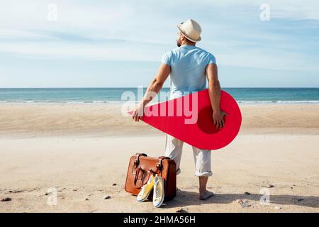 Back view lost male tourist standing with red location pin on sandy beach near sea and searching for direction Stock Photo