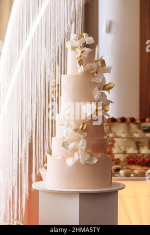 Wedding cake. Close-up photo of a festive beautiful pink five-tiered wedding cake decorated by white and gold flowers. candy bar. Stock Photo