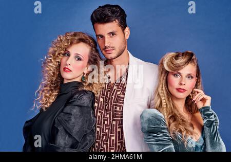 Were going back in time. Shot of three young people posing together in 80s clothing against a blue background. Stock Photo