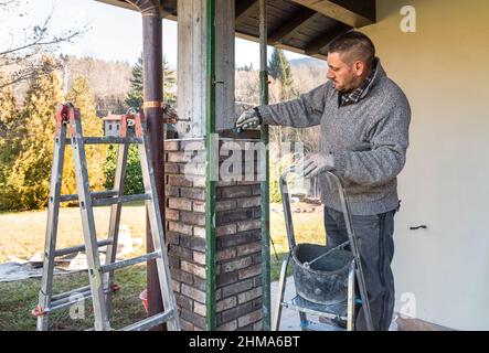 Bricklayer worker installing bricks on the exterior concrete pillar of the house. Construction worker laying bricks. Stock Photo