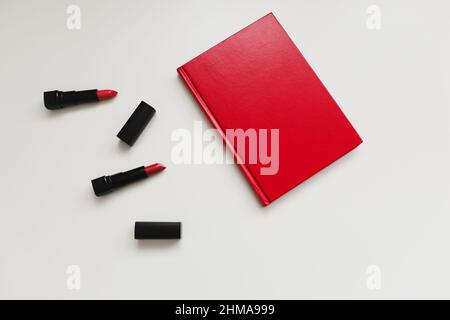 Feminine desk with cosmetics, lipstick and red book or diary on white background. Flat lay, top view. High quality photo Stock Photo