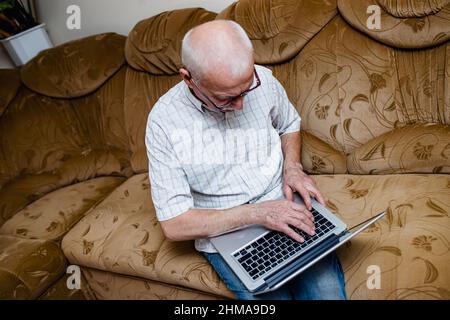 Happy mature senior man in his 60s, having fun studying online. The concept of older technologies. Old man working remotely from home on laptop. Top v Stock Photo
