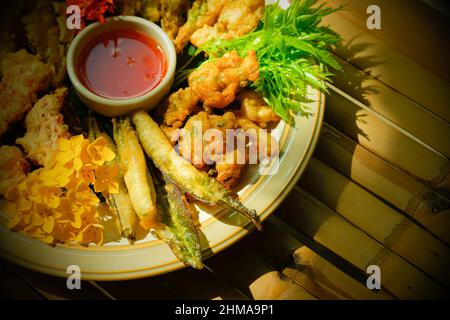 Deep-fried tropical flowers, leaves, and vegetables served on a white plate, flat lay on the bamboo table. Healthy food. Top view. Close-up. Stock Photo