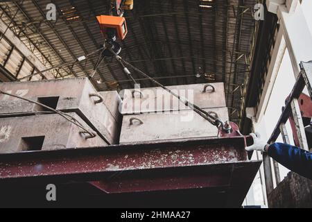 A workman's hands in a glove controlling electric cable hoist, heavy hoist iron hook lifting of structure platform on the large steel box. Stock Photo