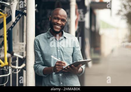 Are you ready to see your bike. Shot of a handsome young man standing alone outside his bicycle shop and writing on a clipboard. Stock Photo