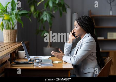 Young afro woman office worker using mobile phone, making phonecall in workplace Stock Photo