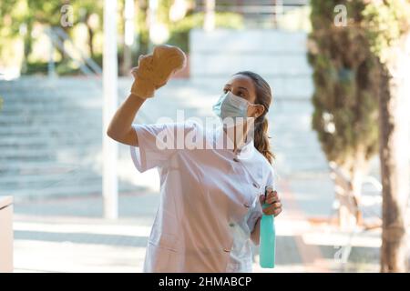 Young woman cleaning windows of clinic on outside Stock Photo