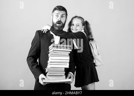Elementary pupil hugging teacher in studio. Father or teacher with school girl daughter hold big stack school textbook notebook books. Teachers day. Stock Photo