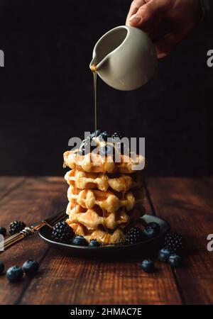 Maple syrup being poured over stack of belgian waffles with berries. Stock Photo
