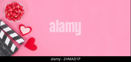 Valentine's Day movie concept. Movie clapperboard with hearts and red caramel popcorn with copy space on pink background. Stock Photo