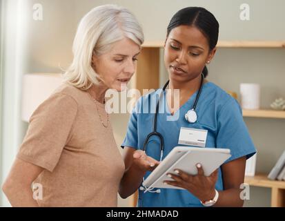 Same expert care from the comfort of home. Shot of a doctor using a digital tablet during a consultation with a senior woman at home. Stock Photo