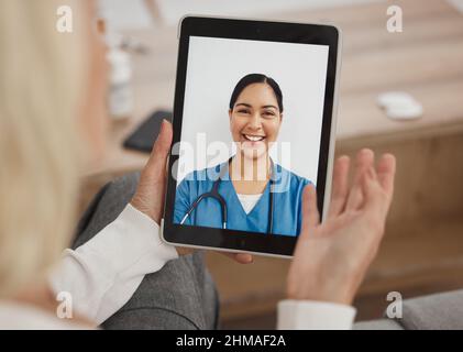 A wireless bridge between doctor and me. Shot of a mature woman using a digital tablet to have a video call with her doctor on the sofa at home. Stock Photo