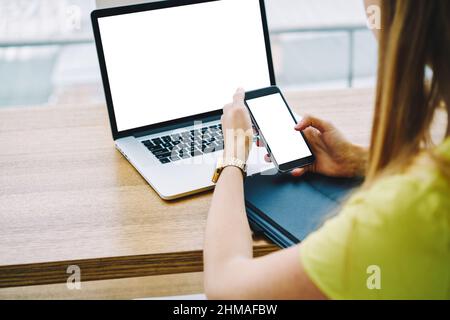 Faceless female freelancer using smartphone and laptop in workspace Stock Photo