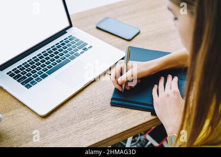 Unrecognizable remote worker using laptop and taking notes in cafeteria Stock Photo