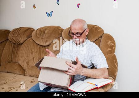 Happy grandfather customer looks into cardboard box with donations. happy age buyer is satisfied with delivery service. Smiling elderly male customer Stock Photo