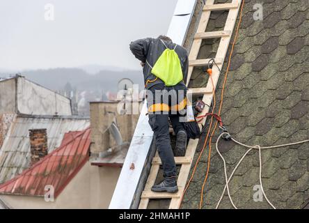 A man works on the roof repair, installs sheet metal on top of the gable wall Stock Photo